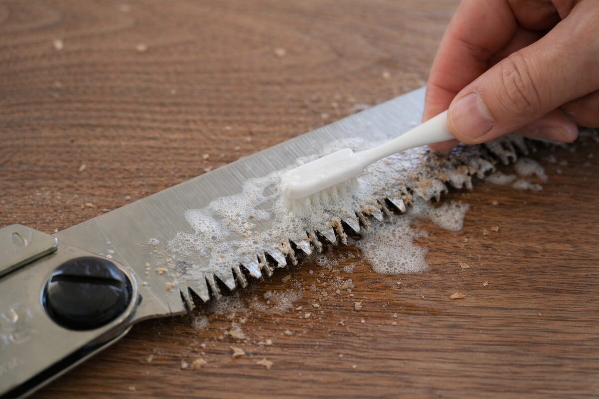 歯ブラシと洗剤を使ってノコギリの刃の汚れを落としている様子